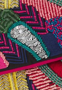 Trabajos de abalorios y lentejuelas de colores brillantes dispuestos en patrones abstractos florales y geométricos sobre una tela oscura.
