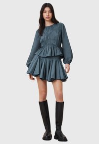 Top peplum blu textured con maniche lunghe, abbinato a una mini gonna svasata a strati. Il modello indossa stivali neri fino al ginocchio.
