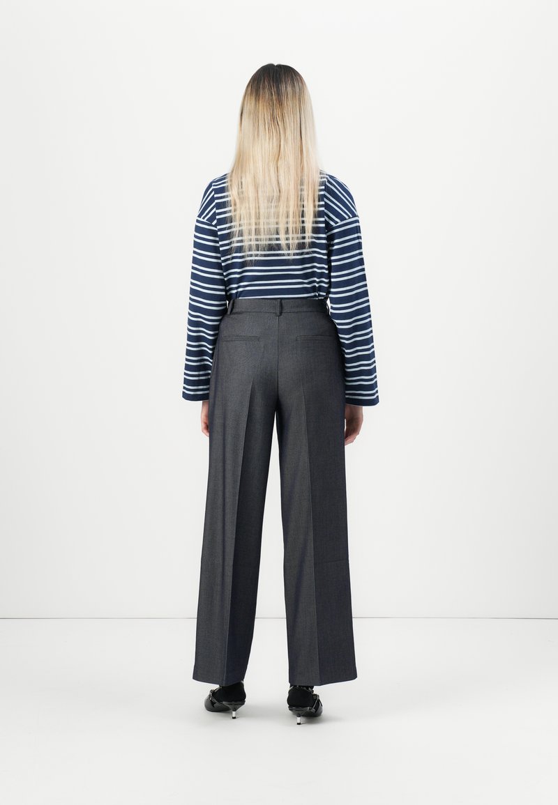 Maglia a maniche lunghe a righe in blu navy e bianco, abbinata a pantaloni grigi a vita alta e gamba larga. L'outfit presenta un design pulito e una vestibilità su misura.