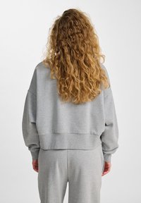 Il pullover grigio corto presenta una vestibilità morbida, maniche ampie e un orlo a costine. Il tessuto sembra morbido con una texture liscia.