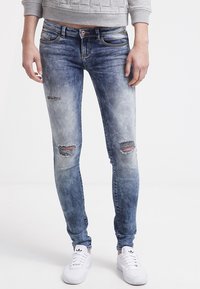 Vaqueros de denim azul de corte ajustado con detalles desgastados, que van de oscuro a claro, con desgarros en las rodillas y diseño de cinco bolsillos.