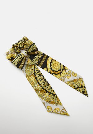 Cachecol de seda com padrão preto e dourado, apresentando um laço e duas extremidades alongadas, adornado com designs florais e ornamentais. Textura suave.