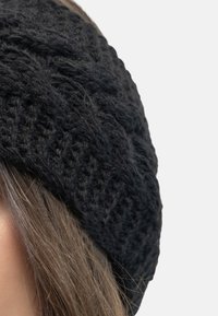 Bonnet en tricot noir avec un motif texturé, doté d'un design ample et d'un tissu doux. Vue en gros plan mettant en valeur les points et la forme.