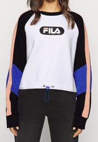 Sweatshirt blanc avec des accents noirs et bleus. Comprend un logo FILA rond, un col côtelé, des manches longues et un ourlet ajustable avec un cordon bleu.
