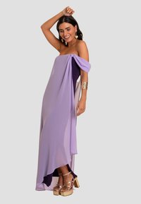 Lavendelfarbenes, schulterfreies Kleid mit drapiertem Stoff, asymmetrischem Saum und dunkelvioletten Akzenten. Kombiniert mit goldenen Plateausandalen.