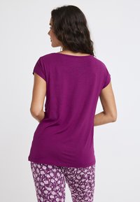 Fioletowa bluzka z krótkim rękawem o luźnym kroju, z okrągłym dekoltem i gładką teksturą, połączona z wzorzystymi fioletowymi spodniami.