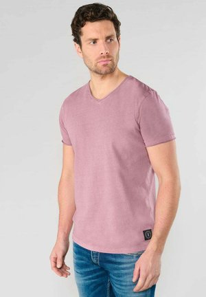 Camiseta de manga corta de color rosa con escote en V, confeccionada en una tela suave y lisa. Etiqueta de marca notable en la esquina inferior izquierda. Combinada con jeans azules.