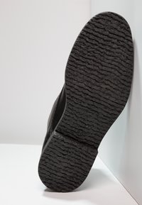 Suela de zapato negra con goma texturizada para agarre. Presenta una forma redondeada y un patrón de relieve claro. Biselado suave con ligera curvatura.