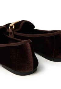 Braune Samt Slipper mit abgerundeter Spitze, flacher schwarzer Sohle und einem metallischen Akzent in der Nähe der Ferse. Weiche Textur und glatte Oberfläche.