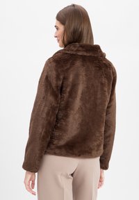 Bruine faux fur jas met een kraag en lange mouwen, met een zachte, gestructureerde oppervlakte. De achterzijde toont een relaxte pasvorm en geen zichtbare sluitingen.