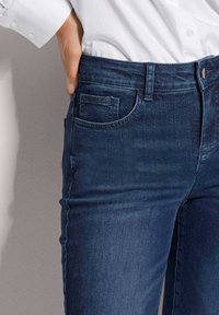 Dark blue denim jeans with a slim fit, featuring a front pocket, belt loops, and a slightly faded texture near the thigh.