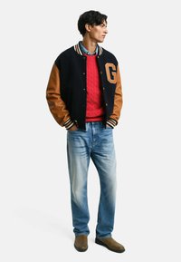 Marineblauwe en bruine varsityjack met een 'G'-letter, rode kabelgebreide trui, lichtblauwe jeans en bruine laarzen. Contrasterende mouwen en geribbelde manchetten.
