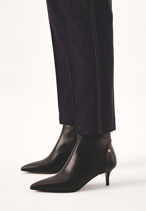 Črne usnjene gležnjarje s koničastim nosom in tankim peto. Gladka tekstura z zlatim logotipom blizu pete. V kombinaciji z temnimi kavbojkami.