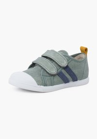Scarpa verde in tela con due cinturini in velcro, strisce blu navy, suola in gomma bianca e una linguetta gialla sul tallone. Presenta un design con punta arrotondata.