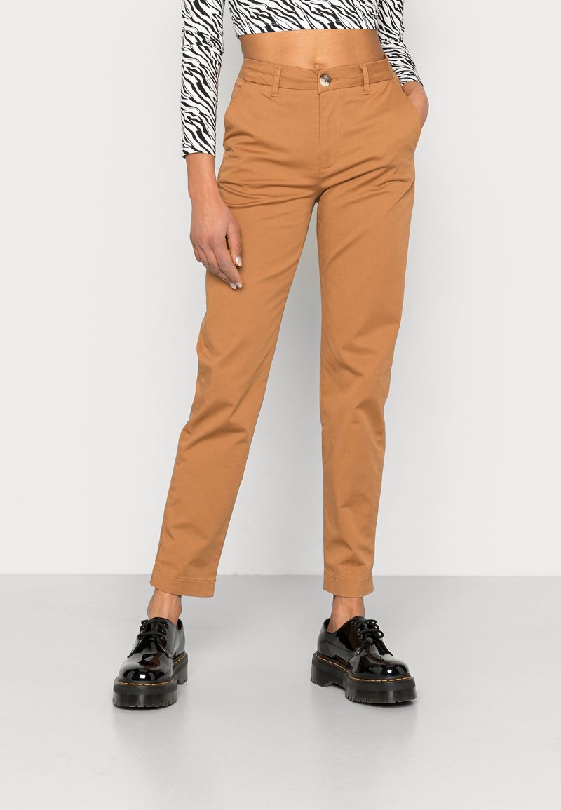 Pantalon slim couleur camel avec poches avant, porté avec des chaussures noires épaisses à lacets et un top court imprimé zèbre.