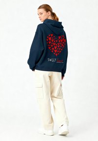 Felpa con cappuccio blu navy con un motivo a cuori rosse con cuoricini; la scritta "SWEET heart" stampata sotto. Abbinala a pantaloni cargo crema e sneakers bianche.