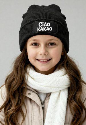 Black knitted beanie with "Ciao Kakao" patch, worn with a white textured scarf and beige jacket, featuring a zip closure.