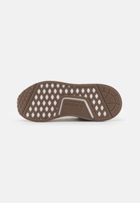 Brown sneaker outsole with a patterned design, featuring hexagonal cutouts and textured rubber for grip. "adidas" logo visible.