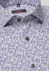 Camicia bianca con un motivo floreale blu e giallo. Presenta un colletto a punta e bottoni marroni. L'etichetta riporta "Eterna Modern Fit".