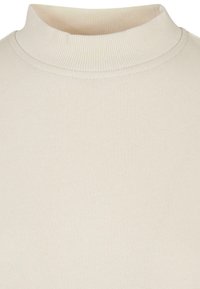 Gräddfärgad topp med hög hals tillverkad av mjuk, strukturert tyg. Ribbad krage och slät kropp, lämplig för lager-på-lager eller avslappnad användning.