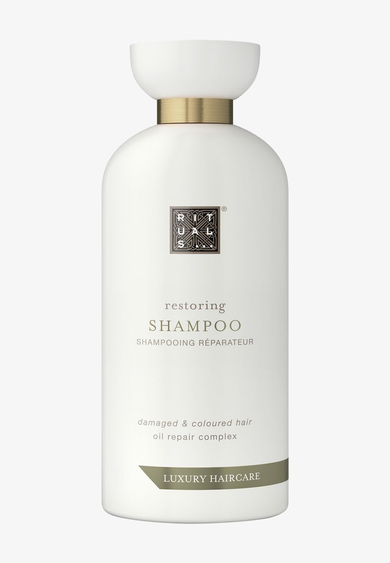 Bouteille cylindrique blanche avec un capuchon doré, étiquetée "Shampoing Restaurateur" pour les cheveux abîmés et colorés, présentant un design épuré et un texte élégant.