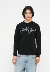 Sudadera negra con cuello redondo, con el logo en cursiva blanca "Jack & Jones" en el pecho. Tejido suave y detalles de puños acanalados.