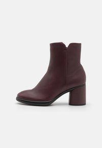 Burgundy nilkkurit, joissa on sileä nahkapinta, pyöristetty kärki ja paksu korko. Varustettu vetoketjukiinnityksellä ja solakalla siluetilla.