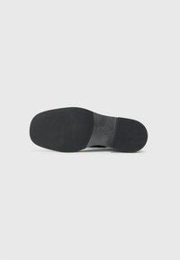 Semelle de chaussure en caoutchouc noir avec une surface lisse et plate, un bout arrondi et un léger talon. Présente un motif de logo embossé près de la section du talon.