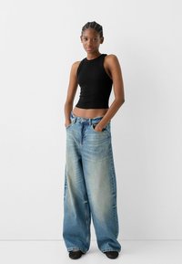 Black sleeveless crop top with a fitted design paired with loose, faded blue denim jeans featuring a high waist and wide leg silhouette.