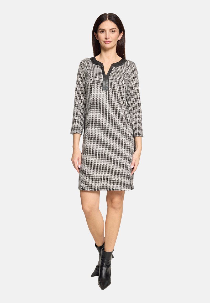 Zwart-wit jurk met patroon, v-hals en driekwartmouwen. Voorzien van een zwart neplederen inzetstuk en zijsplitten. Gecombineerd met zwarte enkellaarzen.