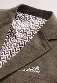 Blazer marron texturé avec doublure en soie blanche, noire et marron à motifs et pochette assortie dans la poche poitrine.
