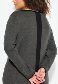 Pull gris foncé avec un panneau arrière texturé noir, des poignets côtelés et une coupe décontractée. Tissu lisse avec un éclat subtil.