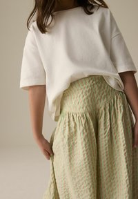 Vit bomull t-shirt med avslappnad passform i kombination med en beige kjol som har vertikala gröna ränder och veck. Släta texturer är uppenbara.