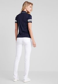Marineblauw poloshirt met witte streepaccenten, korte mouwen; gecombineerd met aansluitende witte broek. Glad materiaal, op maat gemaakt ontwerp.