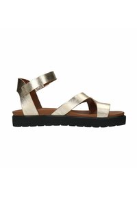 Metalen gouden leren sandalen hebben kruislingse banden, een bruine binnenzool en een zwarte rubberen zool met een gestructureerd profiel.