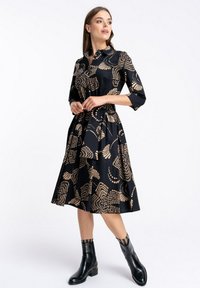 Czarna sukienka z złotymi geometrycznymi wzorami, kołnierzykiem, rękawami trzy czwarte i rozkloszowanym dołem. Połączona z czarnymi botkami za kostkę i tekstylnymi skarpetkami.