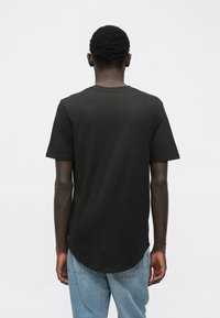 Černé tričko s krátkým rukávem vyrobené z bavlny, s rovný střih a zaobleným spodním lemem. Nosené s světle modrými džíny.