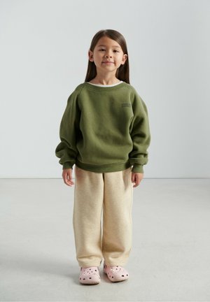 Zelená mikina s rebrovanými manžetami, béžové tepláky a ružové dreváky. Mäkká tkanina a voľný strih, mikina s malým logom.