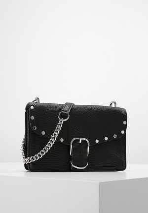 Sac bandoulière en cuir texturé noir avec boucle argentée, détails cloutés et une bandoulière chaîne argentée sur un piédestal blanc.