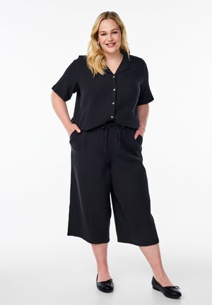 Black two-piece outfit made of textured fabric. Short-sleeved button-up top with a collar and loose, cropped pants featuring an elastic waistband.