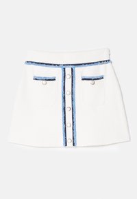 Witte mini-jurk van gestructureerde stof, met twee voorzakken, blauw en marineblauwe accenten, en een centrale rij metalen knopen.