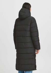 Čierny prešívaný kabát s kapucňou, disponujúci dlhými rukávmi. Kabát má bočné rozparky a voľný strih.
