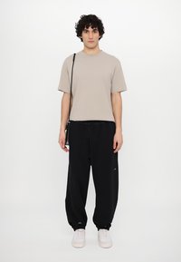 Beige short-sleeve t-shirt, relaxed fit, paired with black jogger pants featuring elastic cuffs and drawstring waist. White sneakers included.
