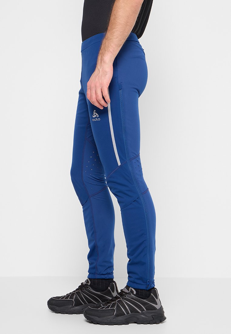 Niebieskie sportowe spodnie o dopasowanym kroju, wykonane z gładkiego, elastycznego materiału z siateczkowymi detalami i odblaskowymi paskami po bokach.