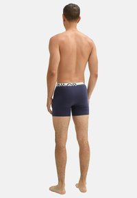 Boxer-briefs bleu marine avec une ceinture élastique blanche à logo, présentant un design ajusté et une texture lisse, affichés de dos.