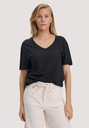 Blonde woman wearing a black V-neck short sleeve T-shirt tucked slightly into light beige high-waisted pants with a tied belt.