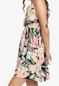 Robe florale avec un haut noué, dans des teintes de rose pastel, vert et noir ; taille élastique ; jupe courte évasée ; motifs de feuilles et de fleurs.