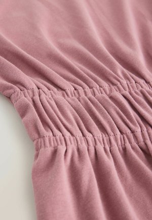 Mīksta rozā auduma ar savilktām šuvēm, kas parāda tekstūru un elastību. Tuvplānā izcelta gluda un nedaudz krokojusies virsma.