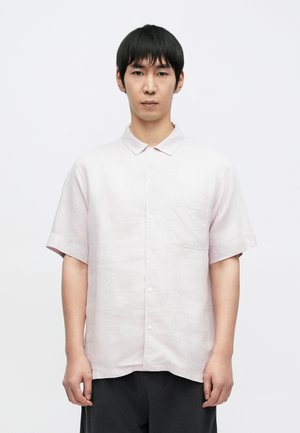 Camisa rosa claro de manga corta con cuello, bolsillo delantero, botones y tela texturizada. Combinada con pantalones gris oscuro.