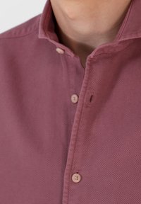 Camicia a maniche corte con colletto in un tessuto a trama viola chiaro, caratterizzata da una chiusura frontale con bottoni beige e una pattina cucita.
